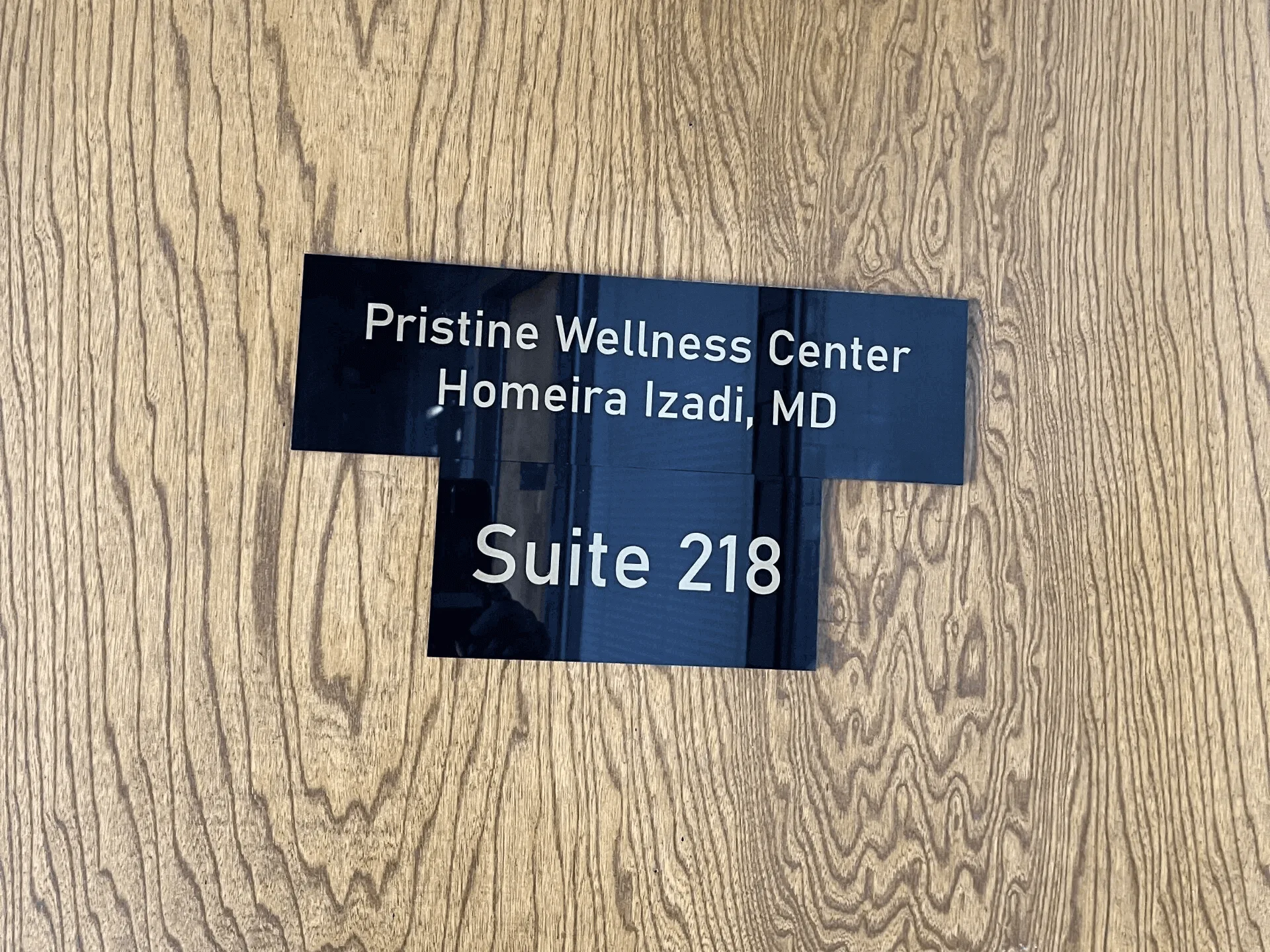 A sign on the wall that says, " pristine wellness center jhomeira izadi, md suite 2 1 8."
