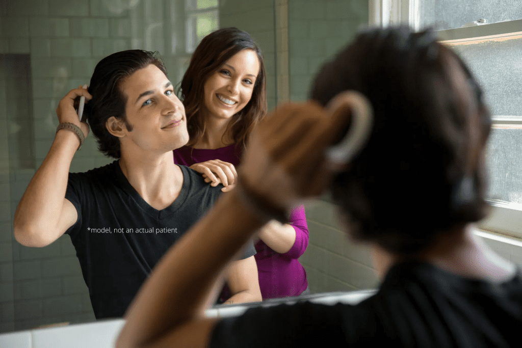 A man is combing his hair in front of two women.