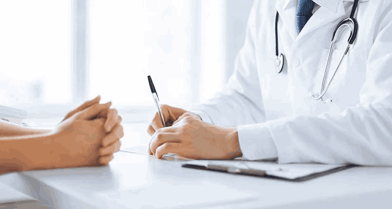 A doctor writing on paper while sitting at desk.