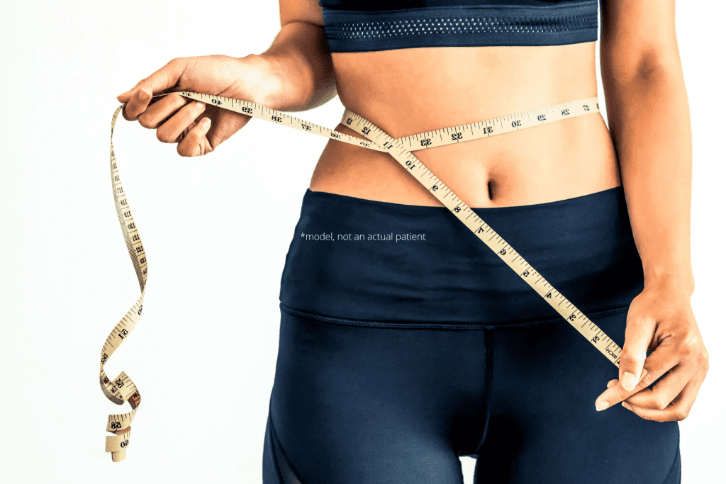 A woman is measuring her waist with a tape measure.