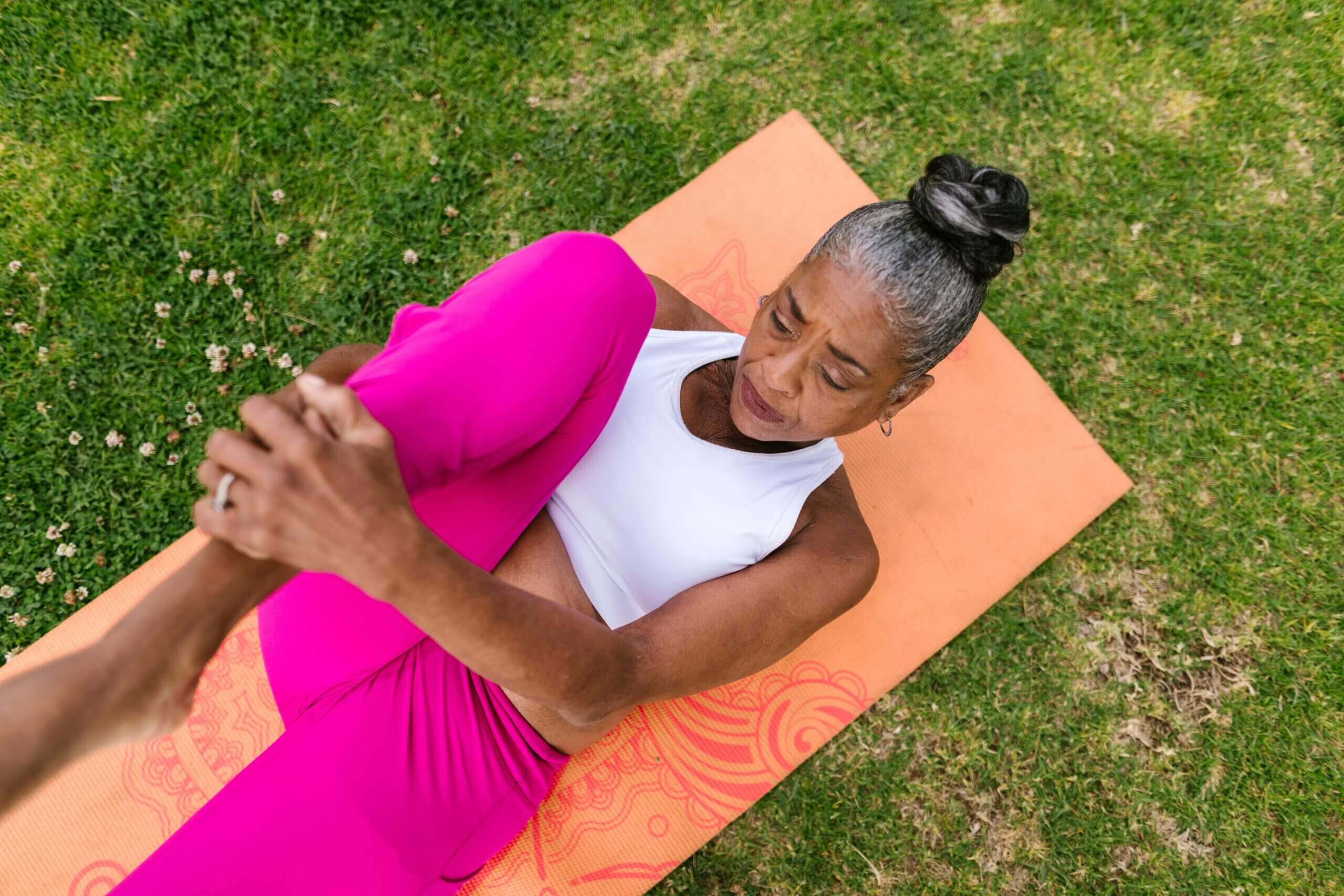 Woman assisted stretching outdoors on mat.